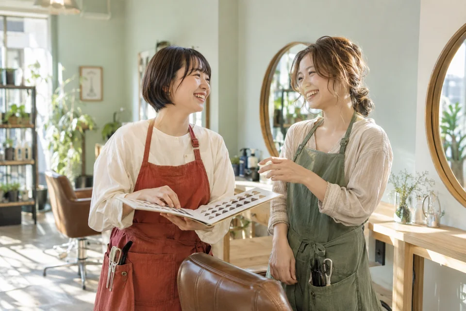 明るいサロンでヘアカラーを相談し合う2人の美容師。AI生成イメージ