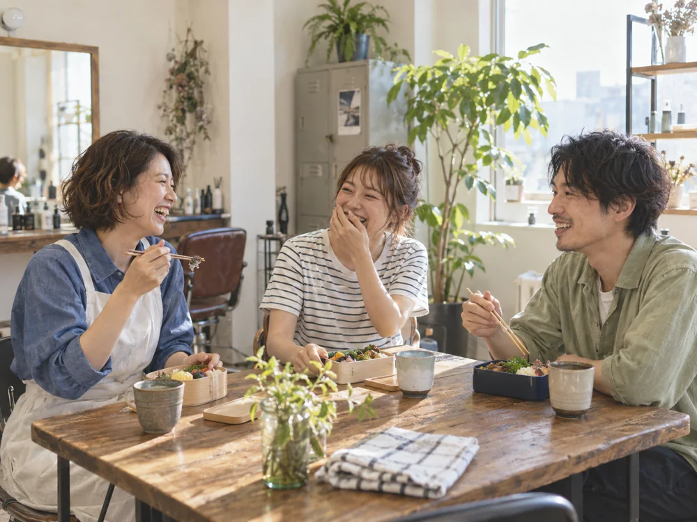 休憩時間にお弁当を囲んで笑い合う、3人の架空のスタッフ
