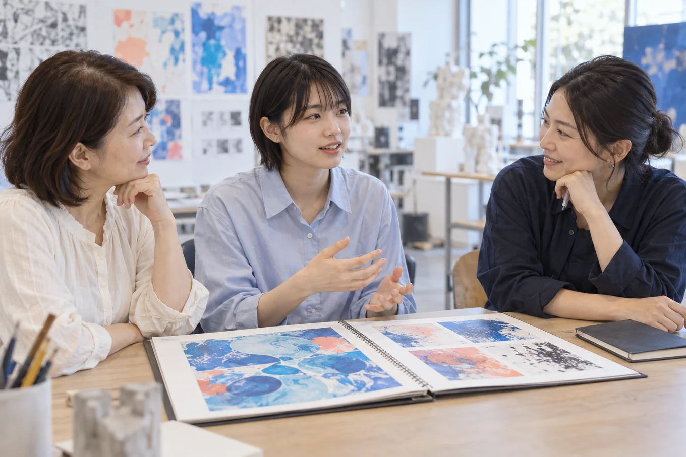 作品集を囲み、進路を検討する学生と保護者が講師と話す相談場面のイメージ
